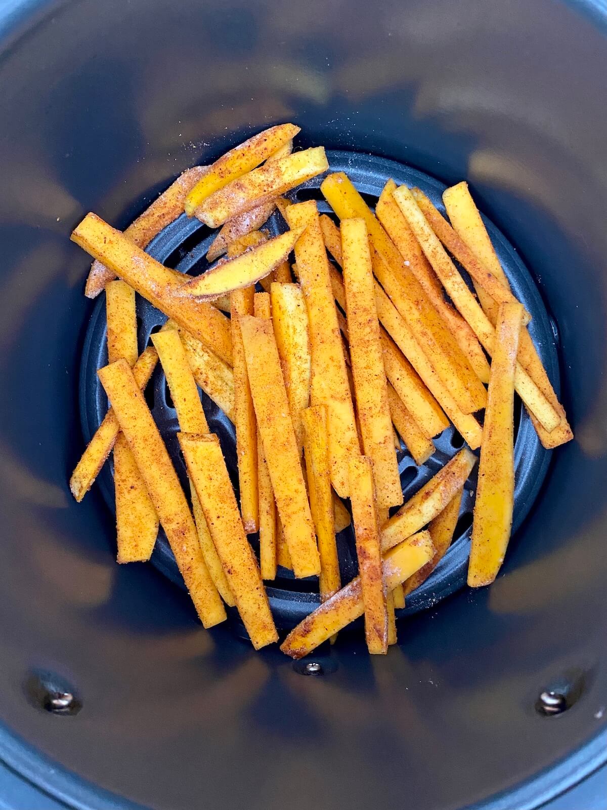 Raw and seasoned butternut squash fries in the basket of an air fryer.