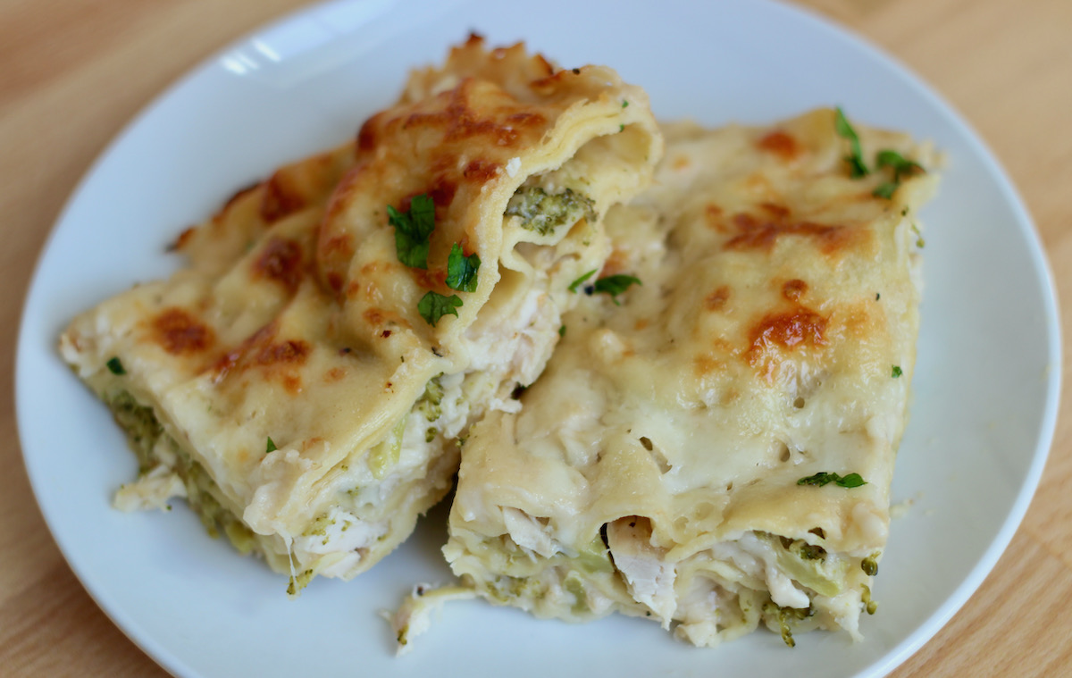 Two pieces of chicken and broccoli lasagna garnished with fresh parsley on a small white plate.
