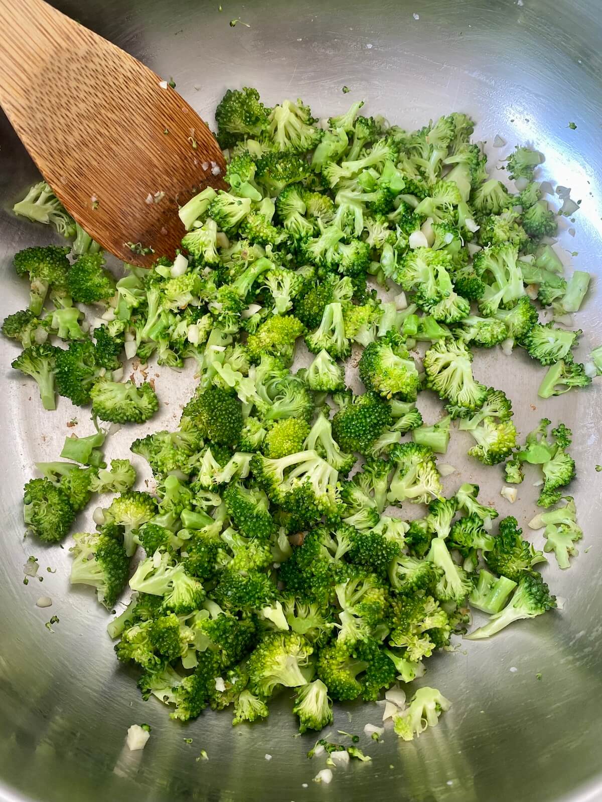 Chopped fresh broccoli and garlic being sautéed in a stainless steel skillet.