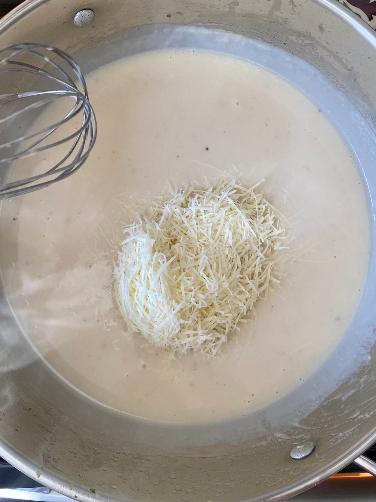 Parmesan cheese sitting on top of a creamy alfredo sauce before being whisked in.