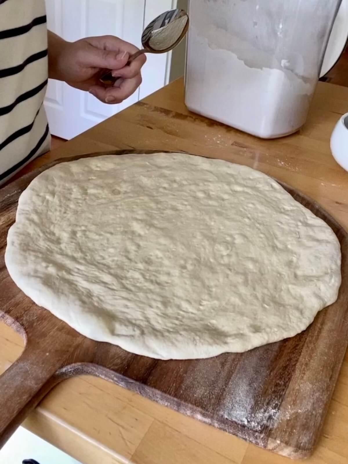 A pizza dough stretched into a large round on a pizza peel.