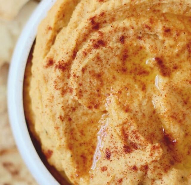 A bowl of roasted butternut squash hummus next to some pita chips.