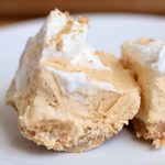 Two no bake pumpkin cheesecake bars topped with whipped cream and crushed graham crackers on a small white plate.