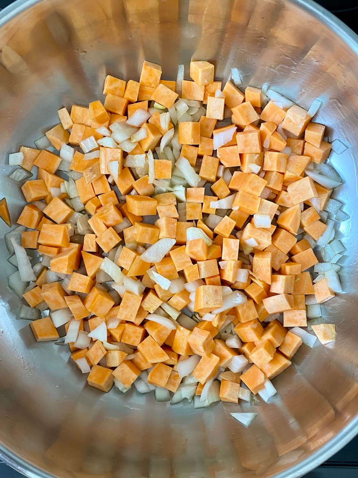 Diced sweet potato and onion being sautéed in a stainless steel skillet.