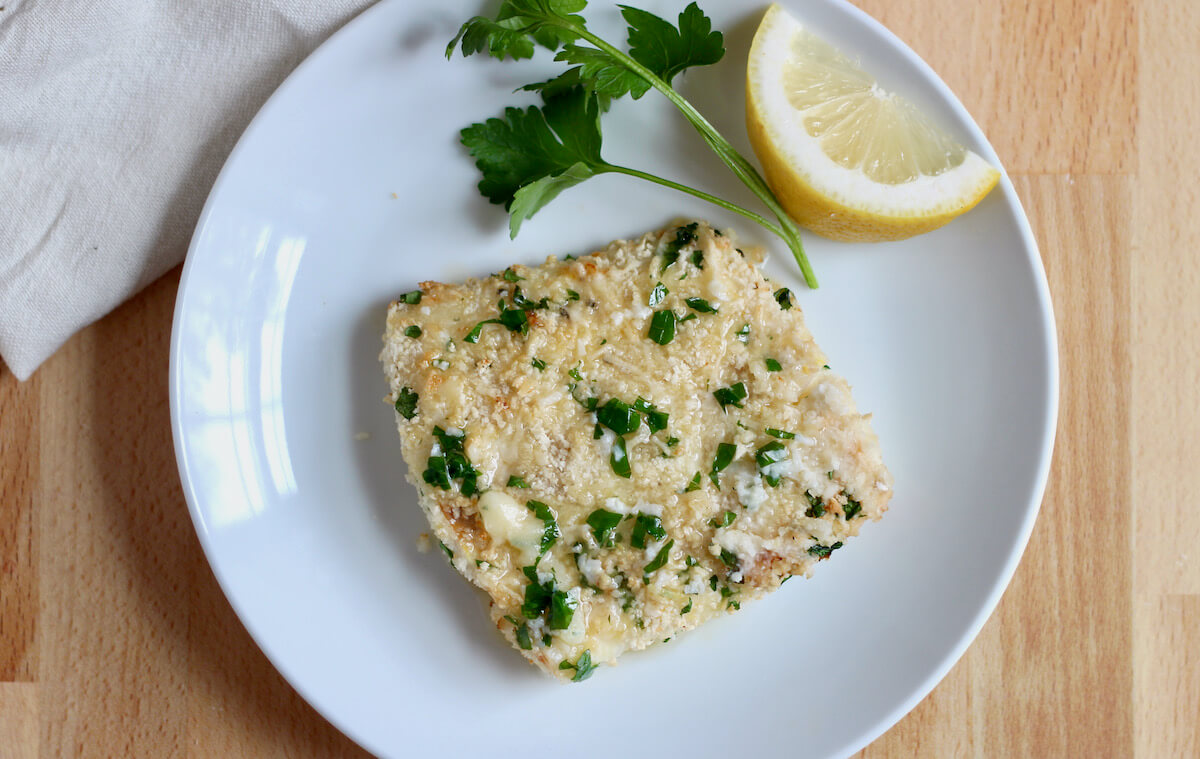 An air fryer halibut filet on a white plate garnished with parsley and a lemon wedge.