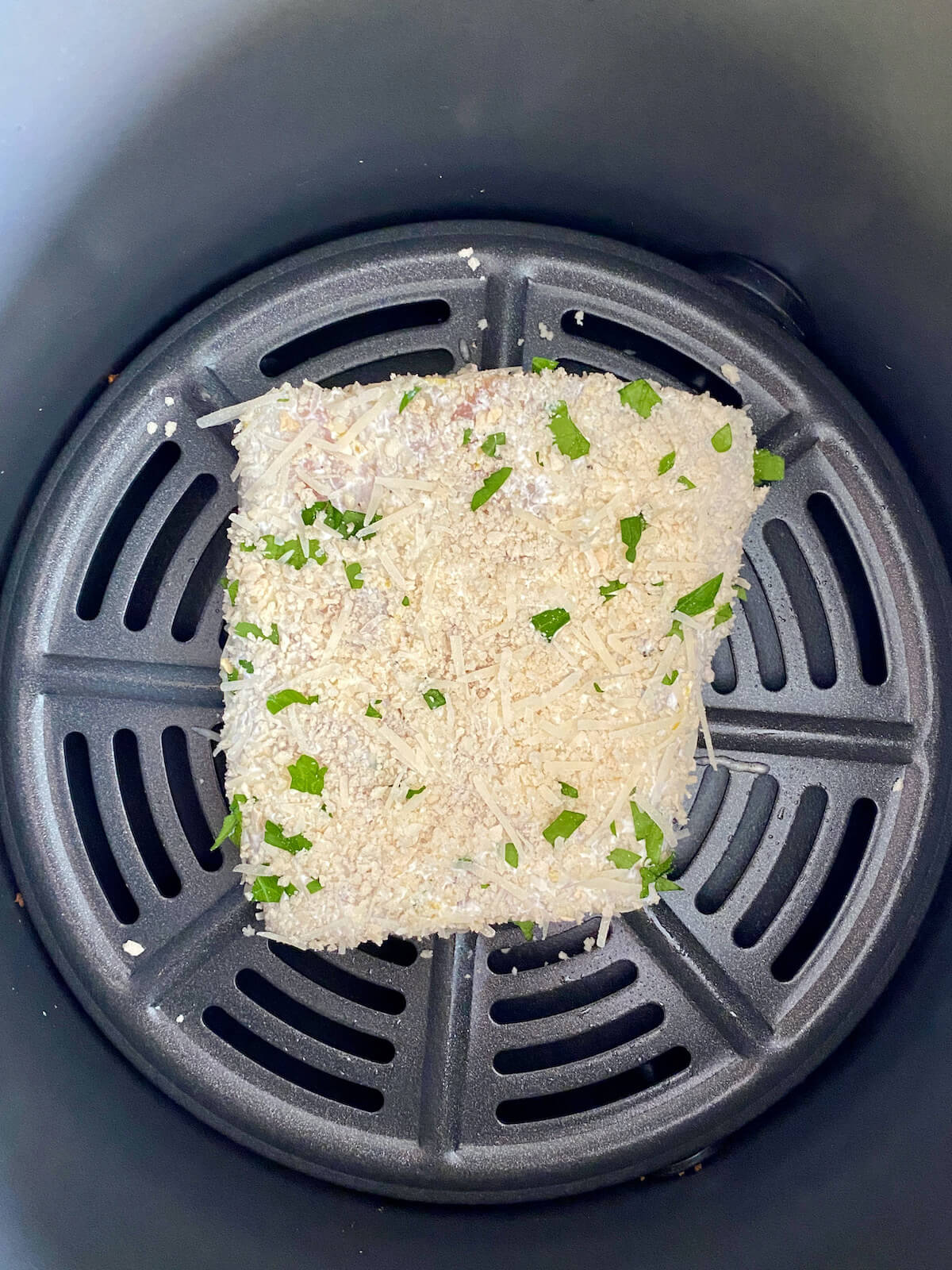 The parmesan-crusted halibut in the basket of an air fryer before being cooked.