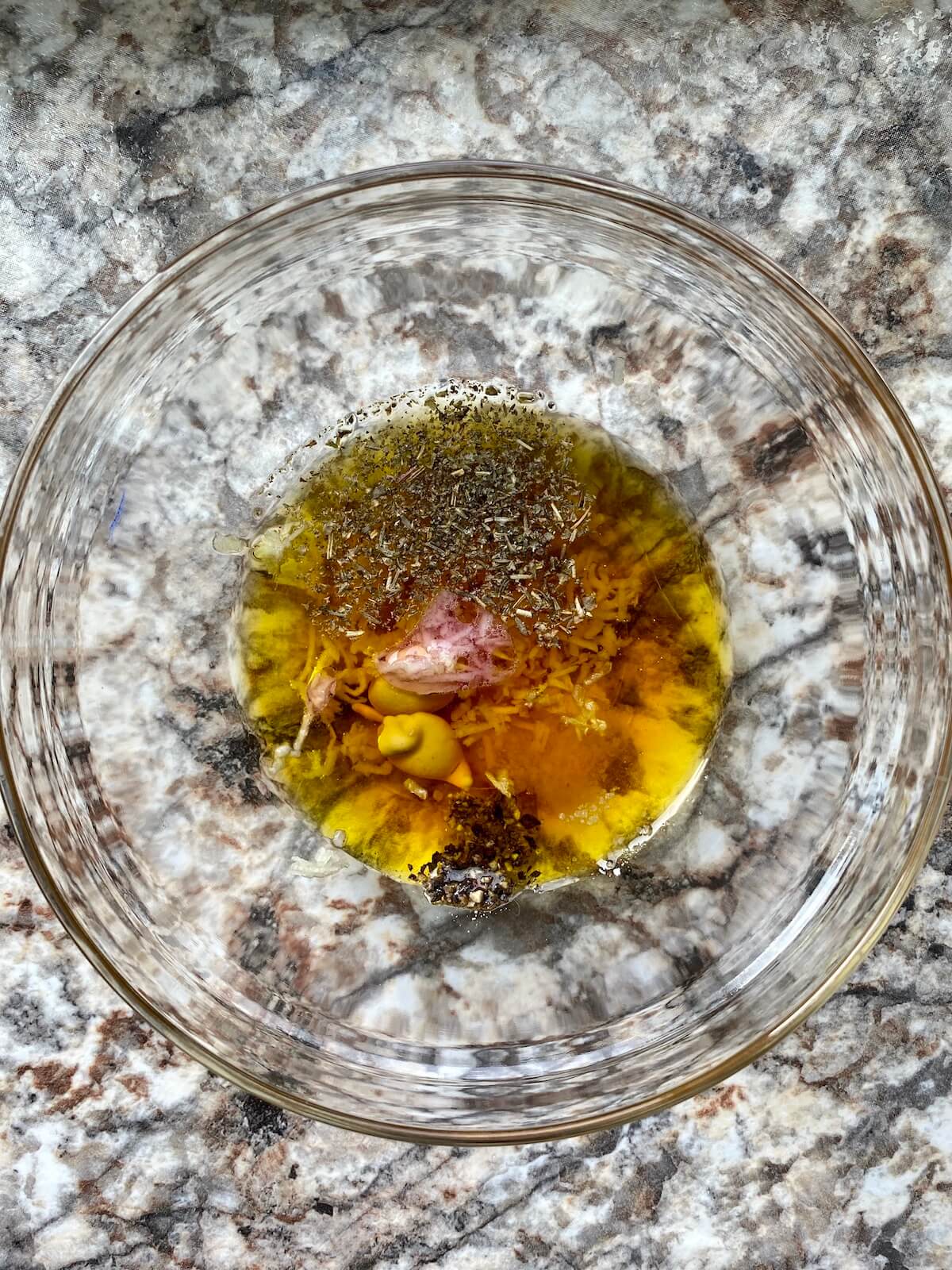 A small glass bowl with the ingredients to make red wine vinaigrette dressing.