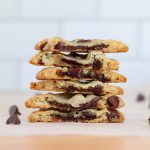 A stack of chocolate filled cookie halves on a sheet of parchment paper.