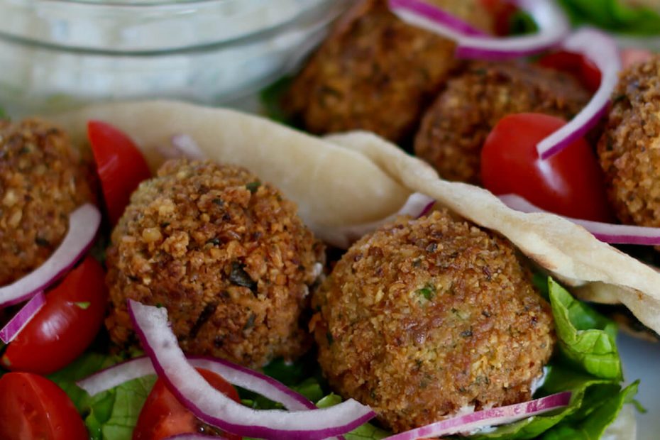 Two falafel gyros on a small white plate. There is a small glass bowl filled with feta tzatziki out of focus in the background.
