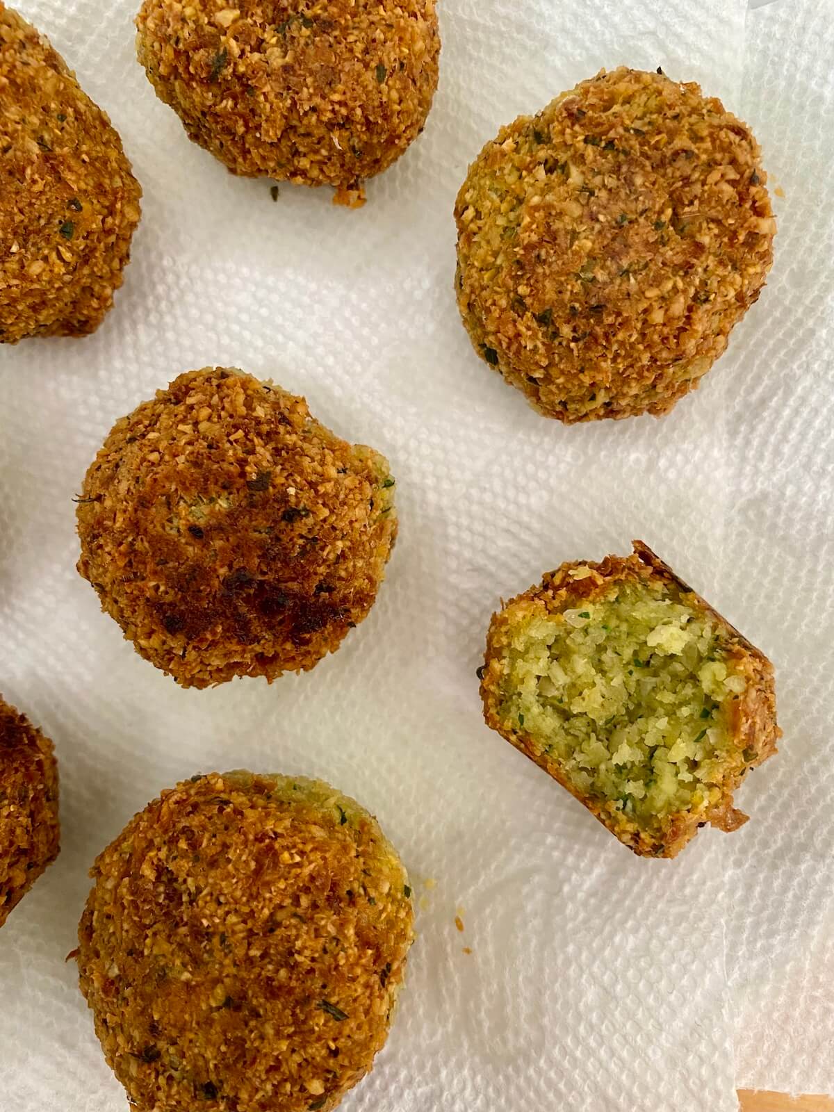 Cooked falafel draining on paper towels. One of the falafel balls has a bite taken out of it.