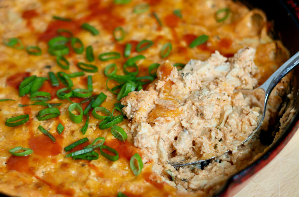 A spoon scooping healthy buffalo dip out of a skillet.