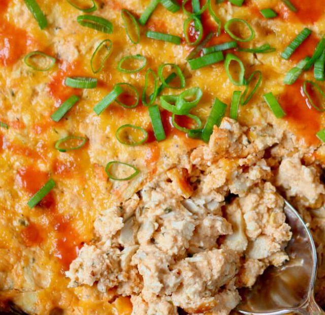 A skillet filled with Greek yogurt buffalo chicken dip. A silver spoon is taking a scoop out of the bottom right corner.