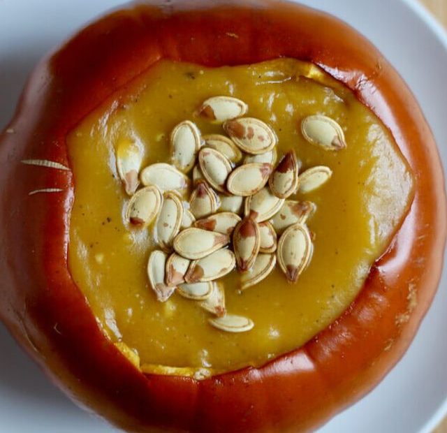A roasted pumpkin bowl filled with roasted pumpkin soup on a small white plate.