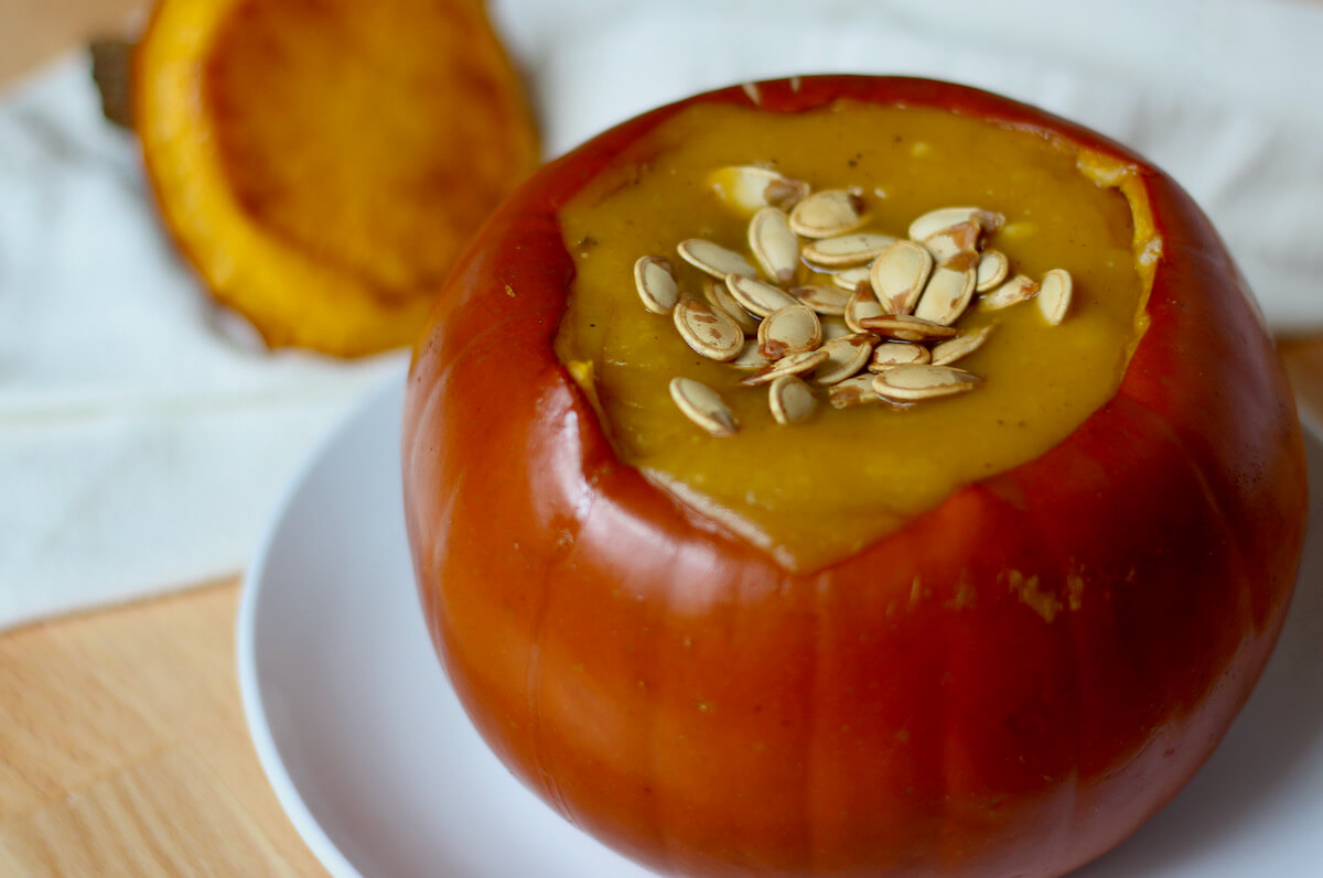 Pumpkin soup dripping out of a roasted pumpkin bowl. You can see the top of the pumpkin out of focus in the background.
