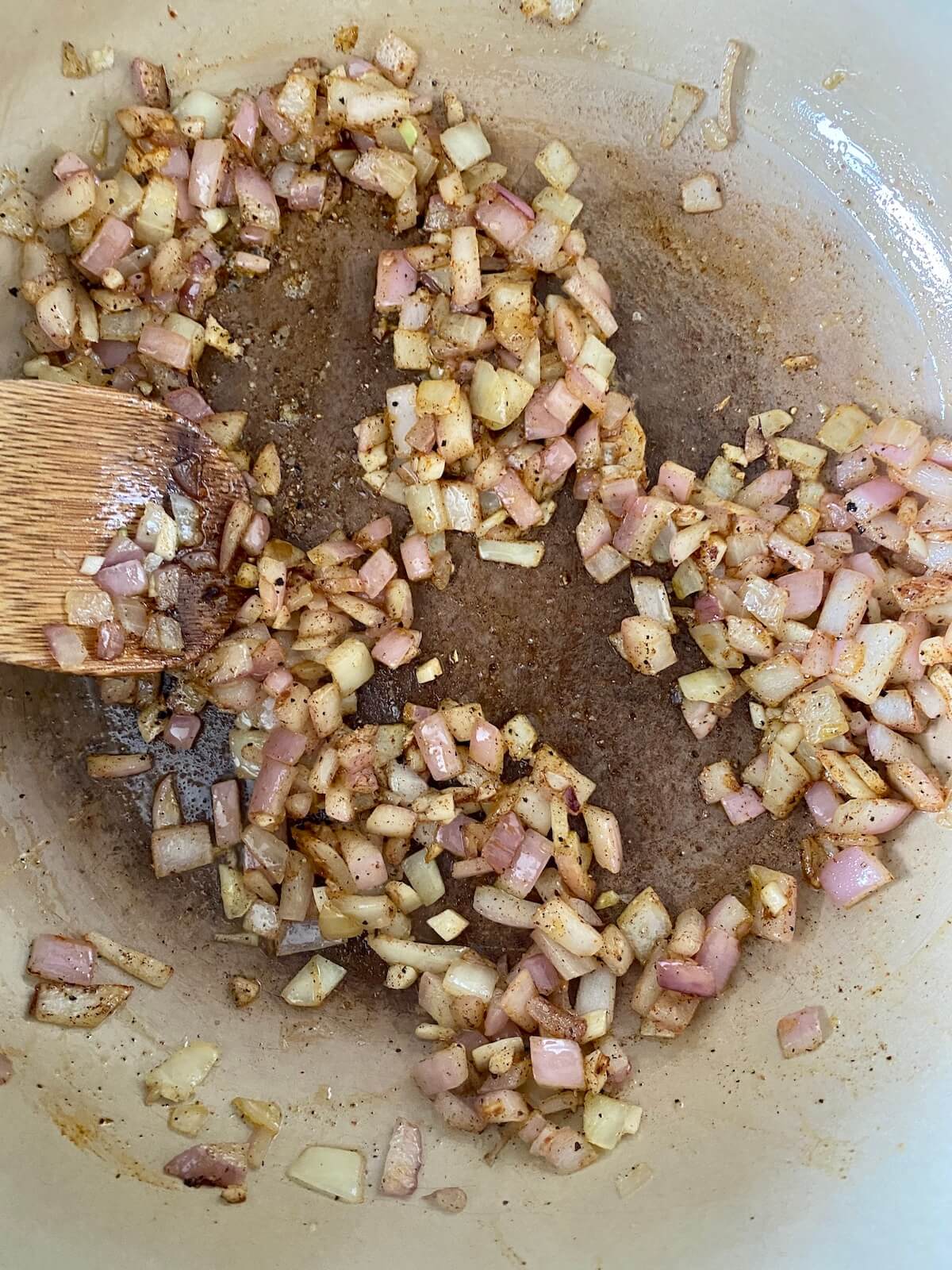 Onion, garlic, cinnamon, nutmeg, salt, black pepper, and cayenne pepper being sautéed in olive oil in a large Dutch oven.