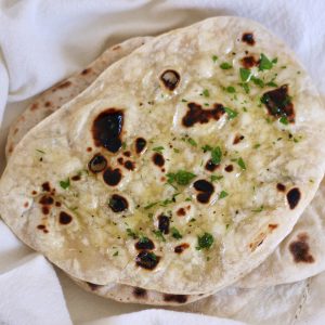 A stack of sourdough discard naan bread garnished with parsley and olive oil on a white cloth napkin.