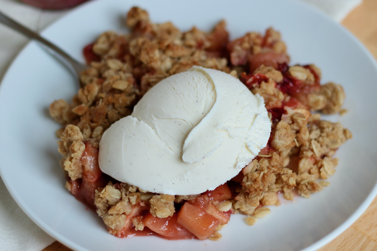 Strawberry apple crisp topped with vanilla ice cream on a small white plate.