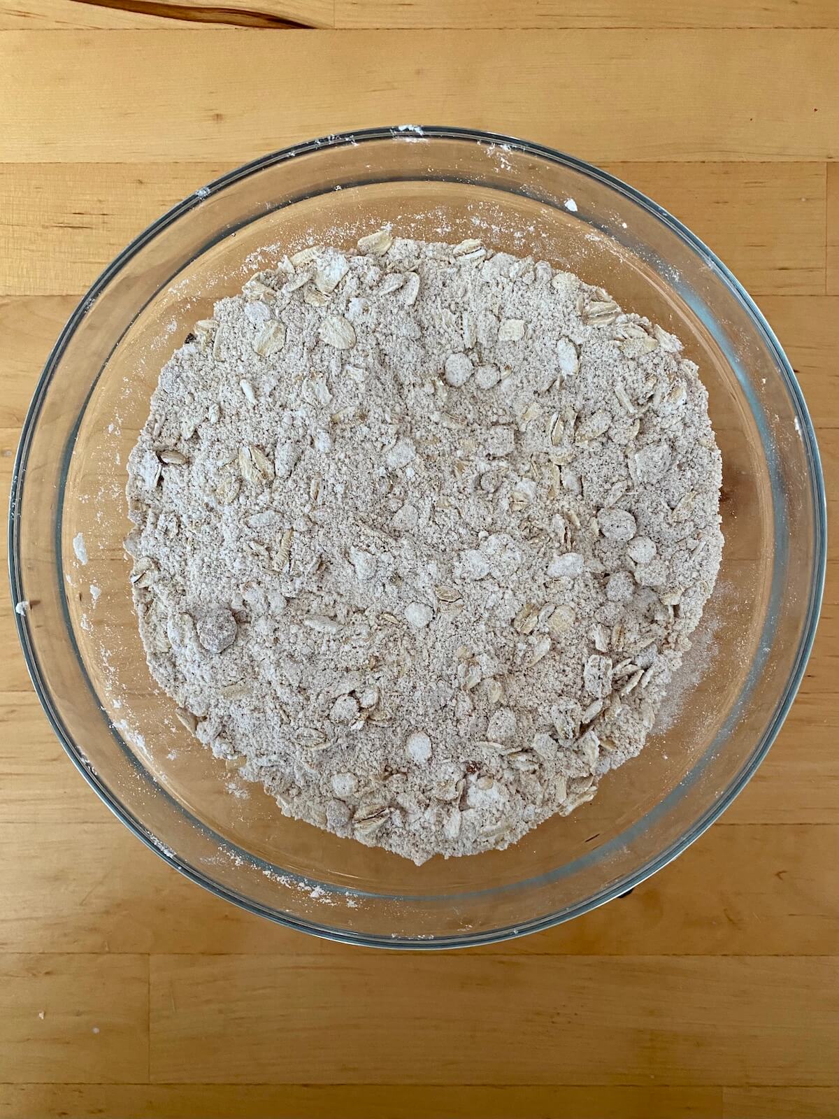 A clear glass bowl filled with the dry ingredients to make the oat streusel crumble.