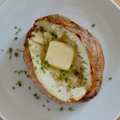 An open baked potato with a pat of butter and chives.