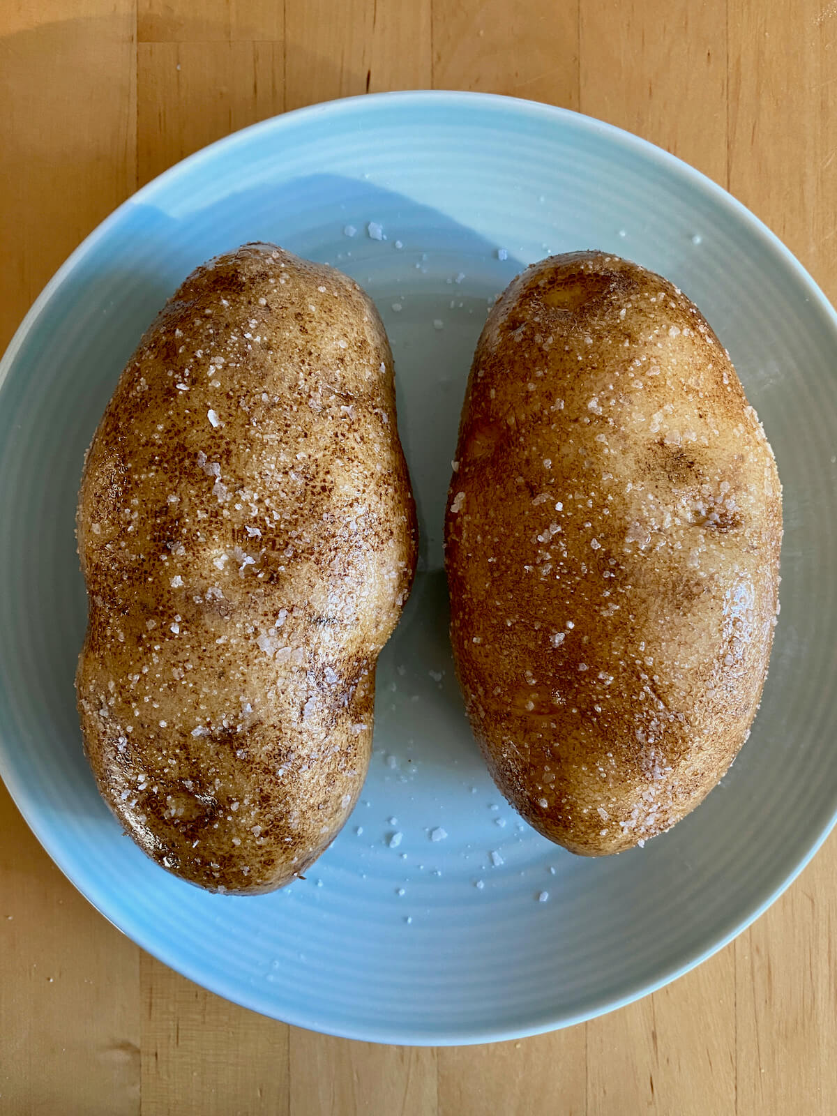 Two raw russet potatoes seasoned with olive oil and salt on a light blue plate.