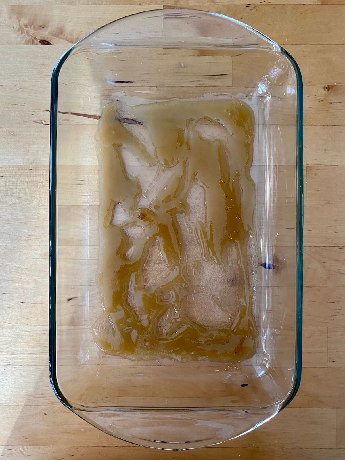 A mixture of melted butter and brown sugar spread on the bottom of a glass baking dish.