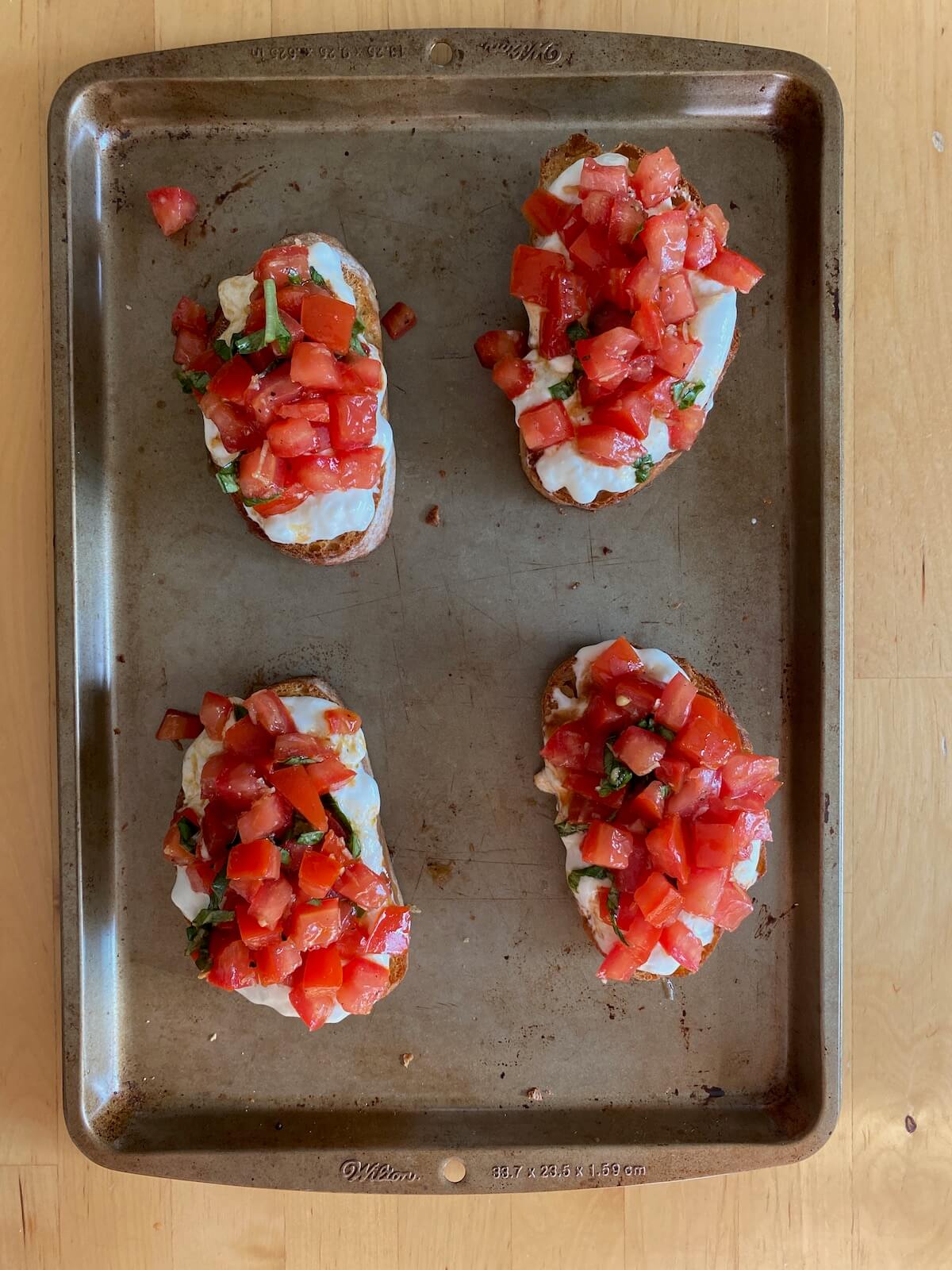 Four fully assembled bruschetta toasts on a rimmed baking sheet.