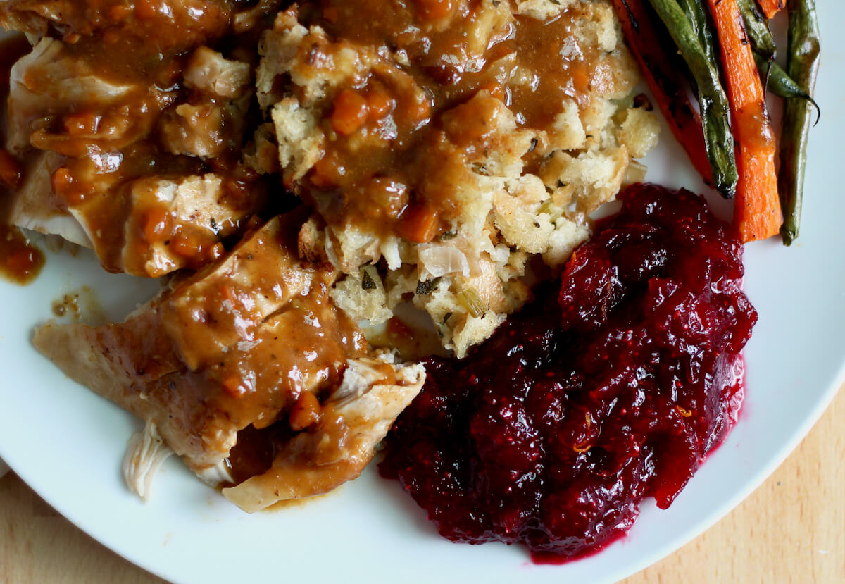 A plate filled with turkey dinner. On the plate is turkey, gravy, stuffing, vegetables, and cranberry sauce.