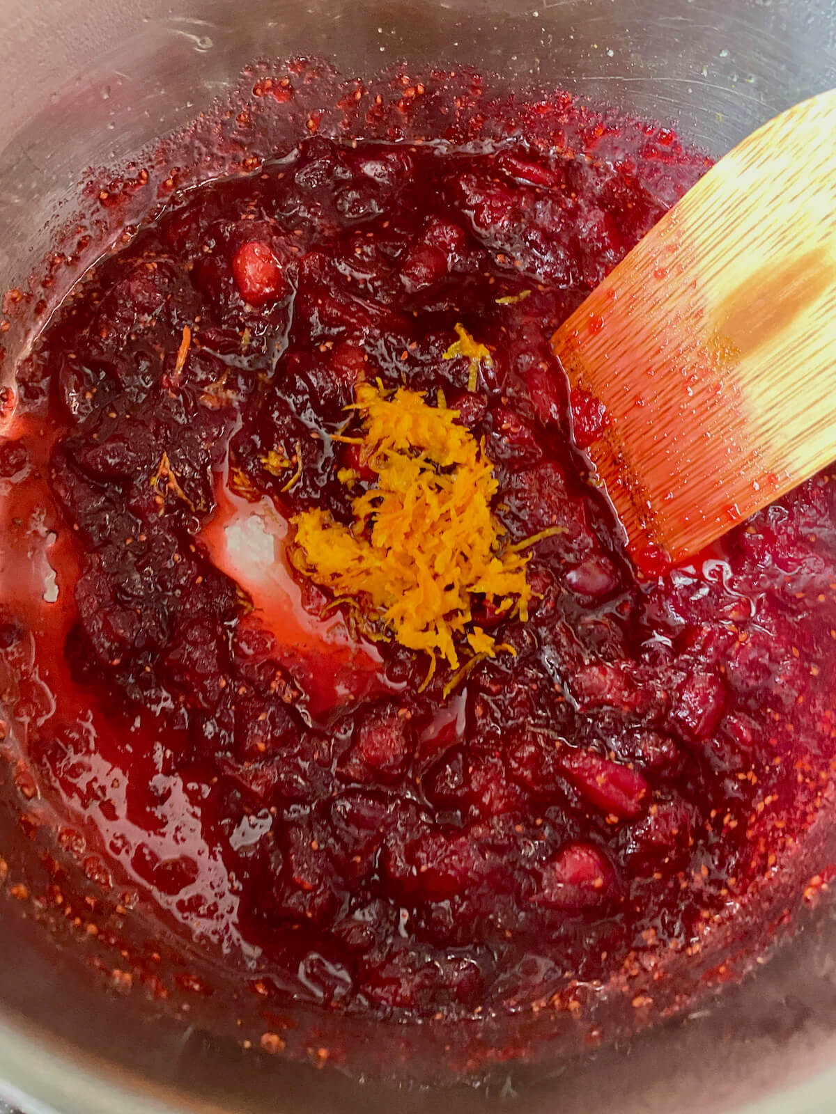 Orange zest being stirred into fresh cranberry sauce with orange juice.