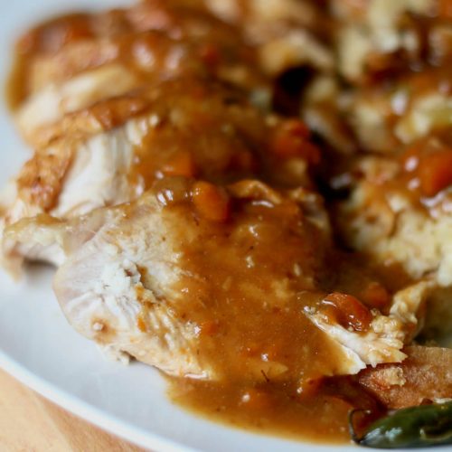 Slices of dutch oven turkey breast smothered in gravy. On the plate next to the turkey is stuffing and green beans.