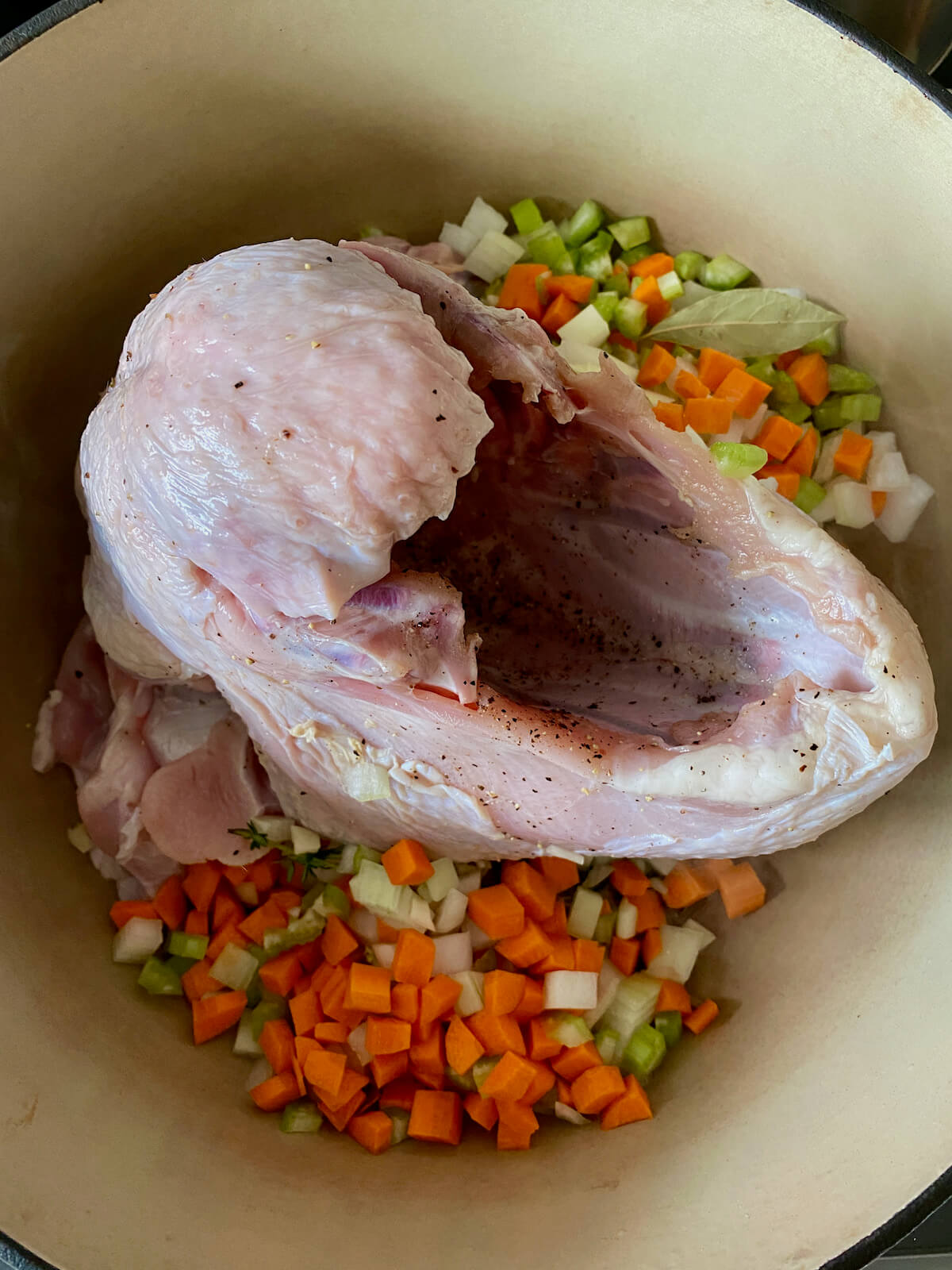 A raw seasoned turkey breast and vegetables just starting to sear in a large dutch oven.