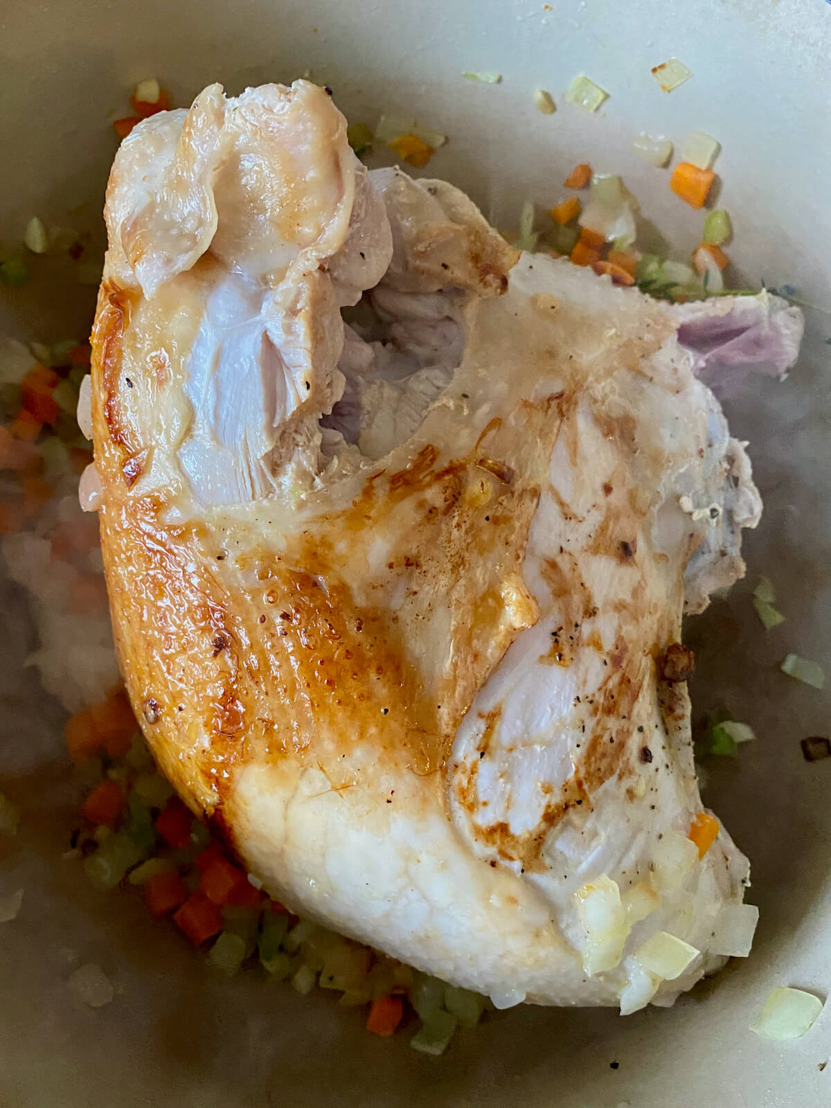 A turkey breast searing in a large dutch oven with vegetables and other aromatics.