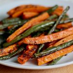 Roasted green beans and carrots on a small white plate.