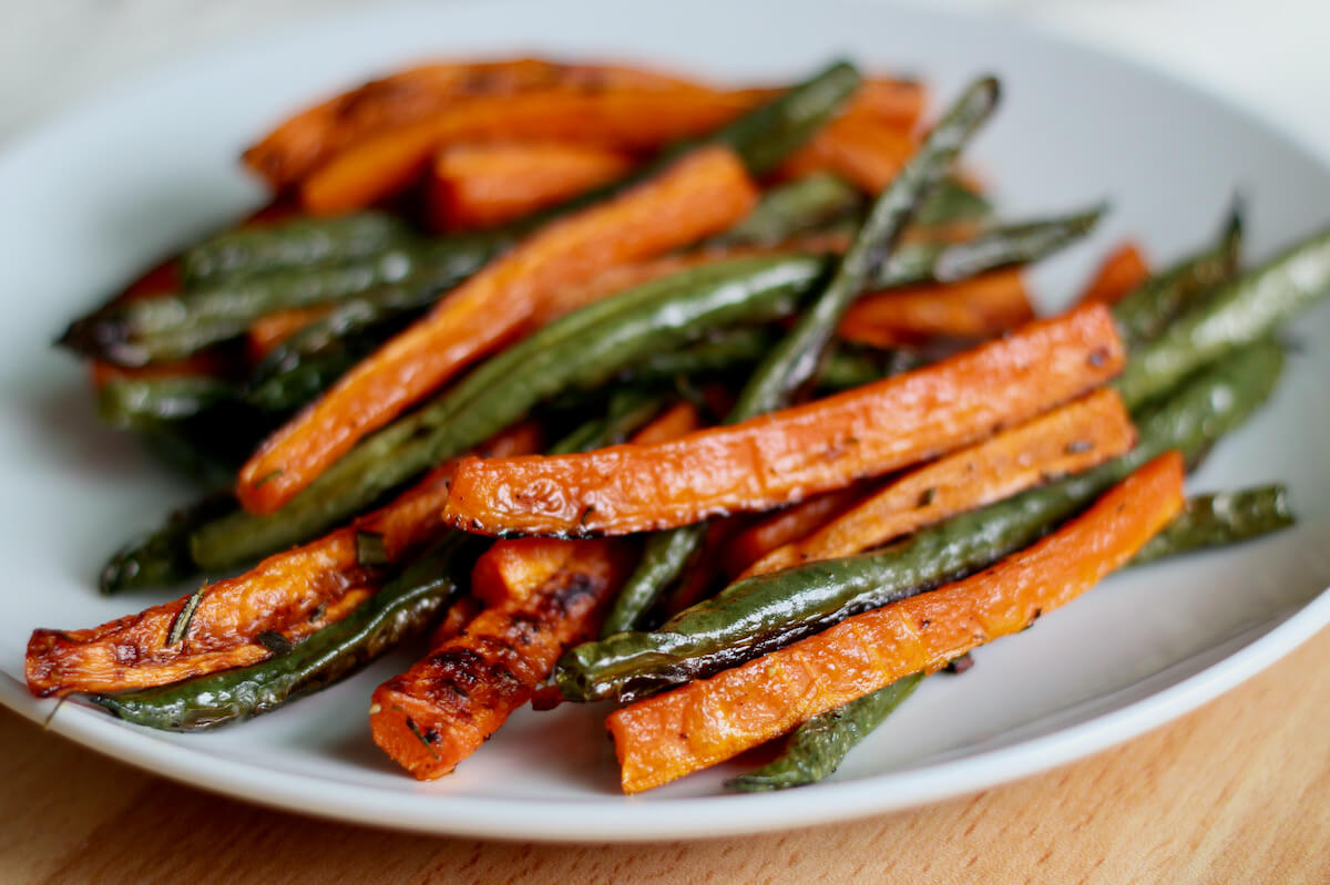 Roasted green beans and carrots on a small white plate.