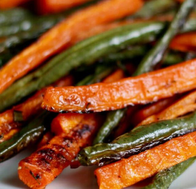 A white plate filled with roasted green beans and carrots.