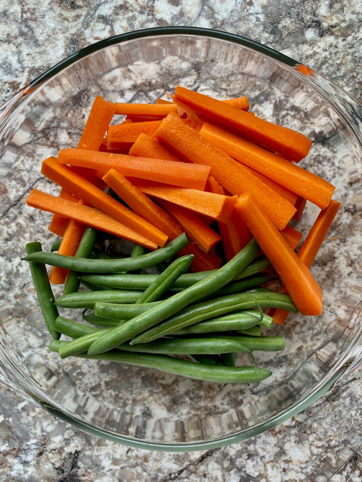 Prepared carrots and green beans in a glass mixing bowl.