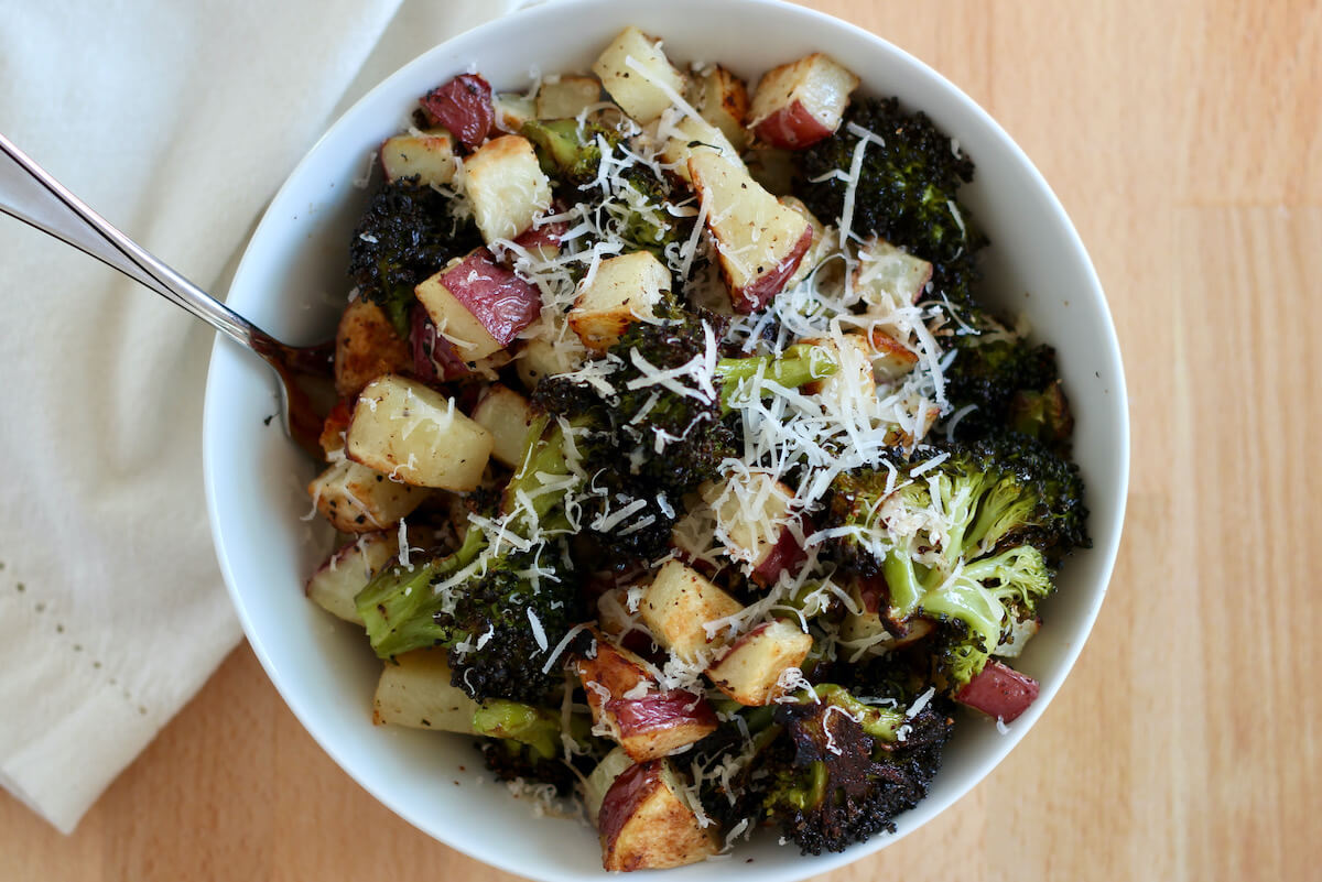Roasted broccoli and parmesan potatoes in a small white bowl. There is a silver fork sticking out of the bowl to the left.