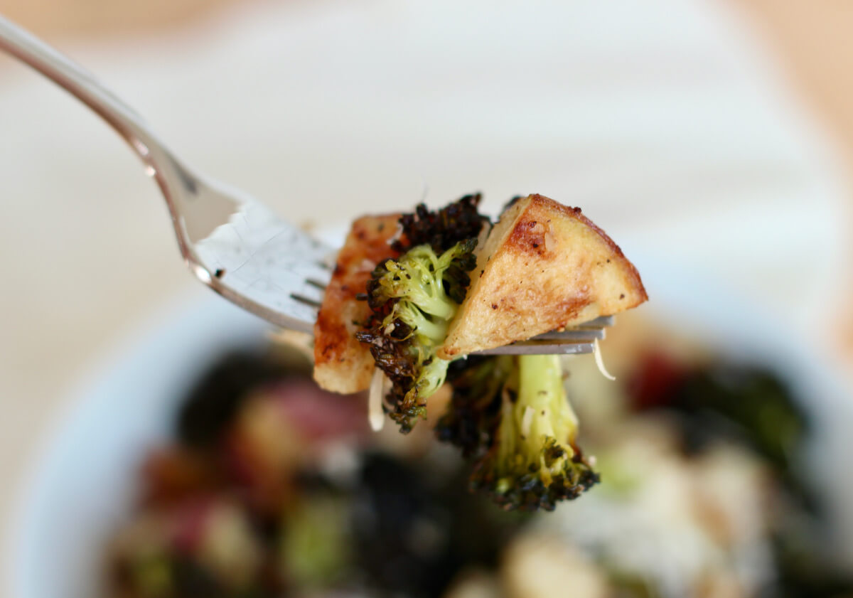 A forkful of roasted potatoes and broccoli being held above a bowl.