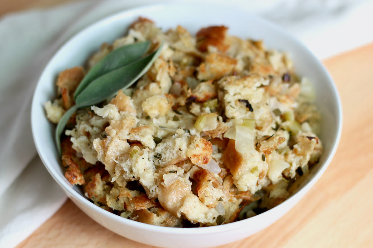 A white bowl filled with sourdough stuffing. The stuffing is garnished with two leaves of fresh sage.