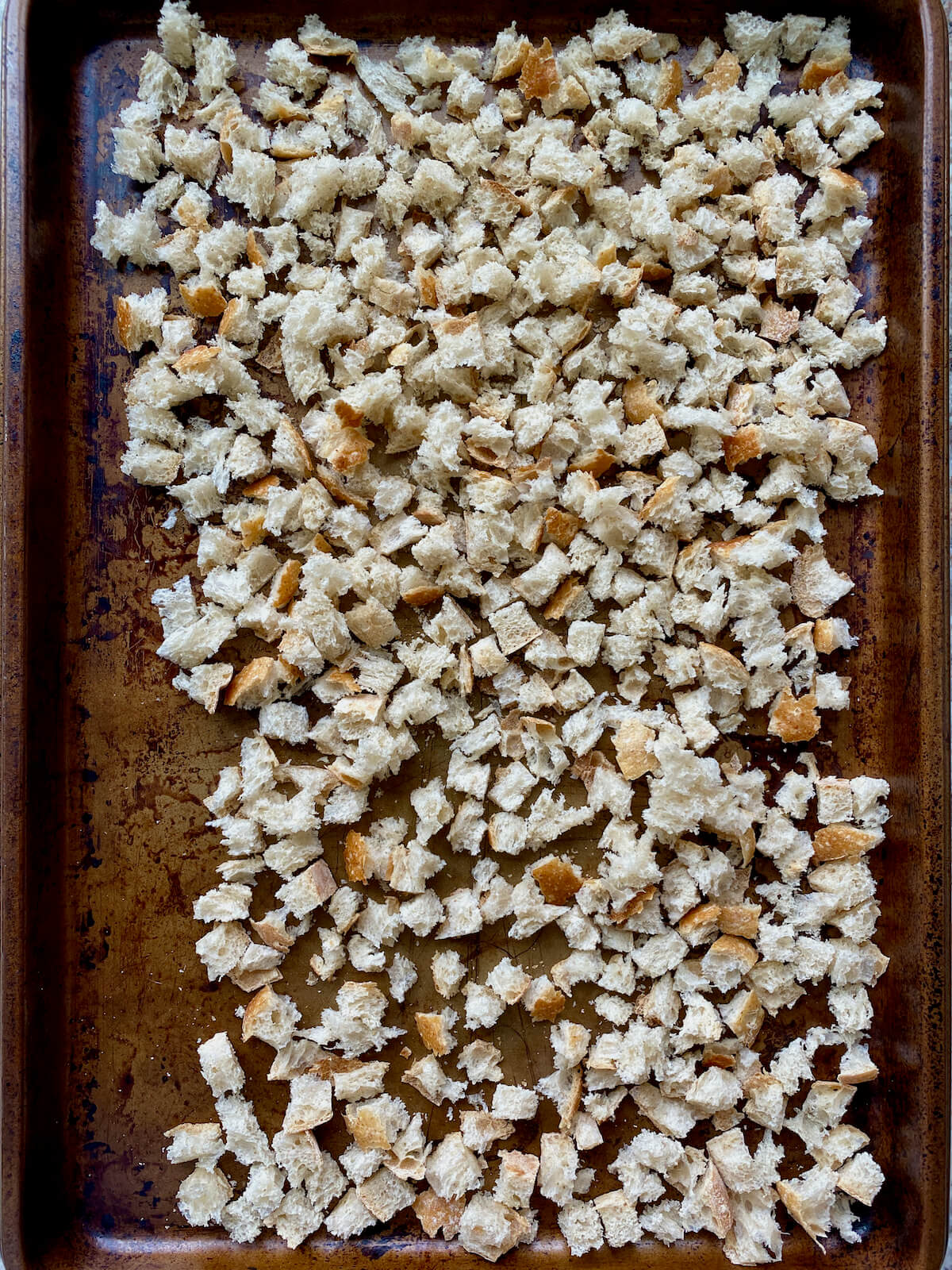 Dried bread cubes on a rimmed baking sheet.