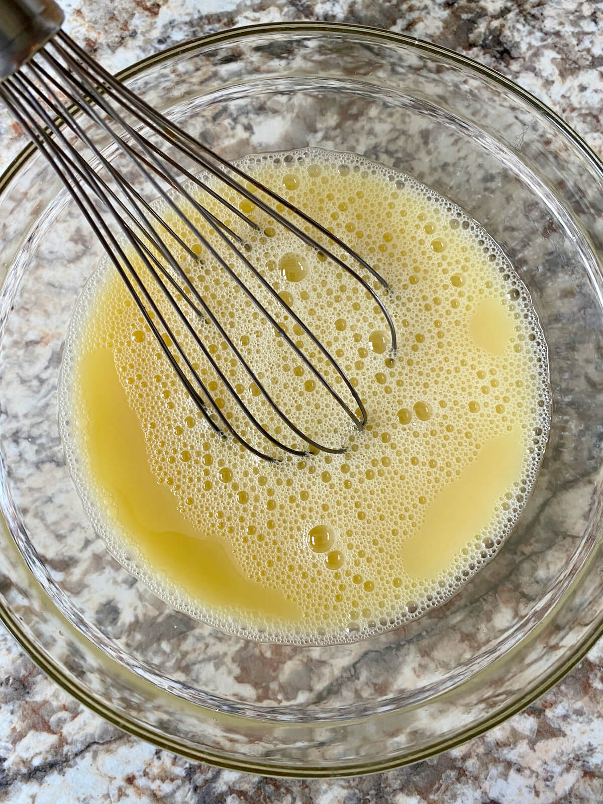 Eggs and chicken stock being whisked together in a clear glass mixing bowl.