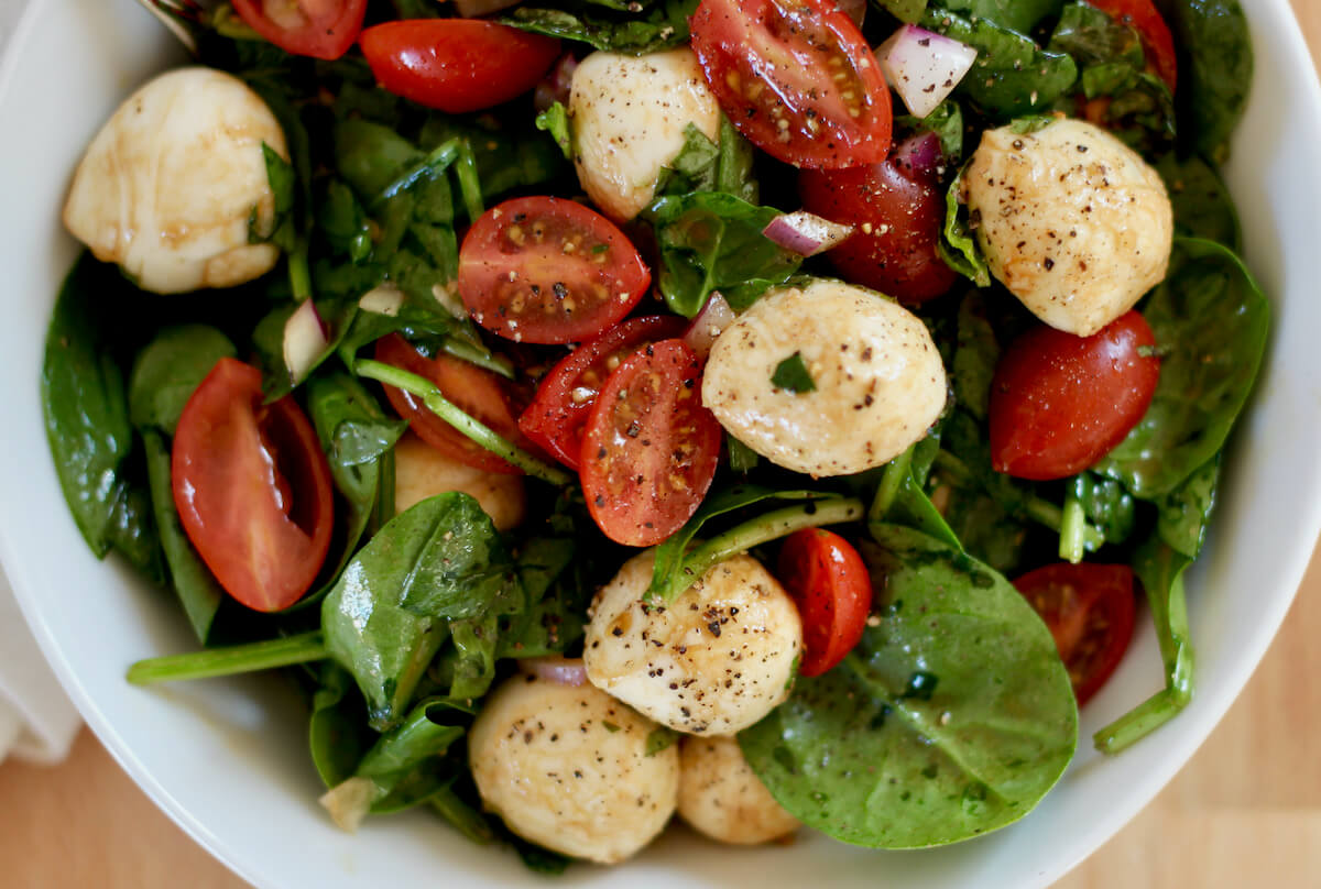A bowlful of spinach caprese salad seasoned with freshly cracked black pepper.
