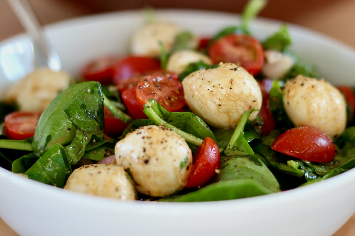 Spinach caprese salad in a small white bowl.