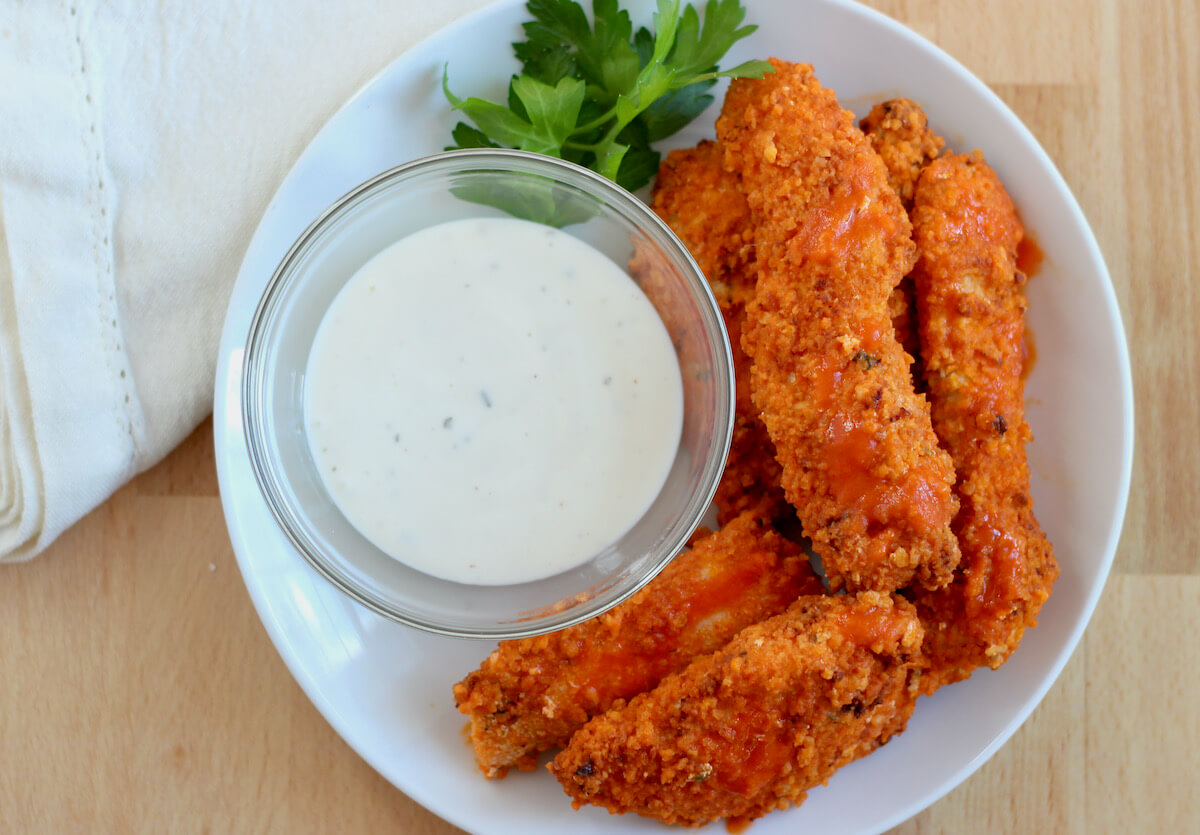 A plate of air fryer buffalo chicken tenders with a bowl of ranch dressing.