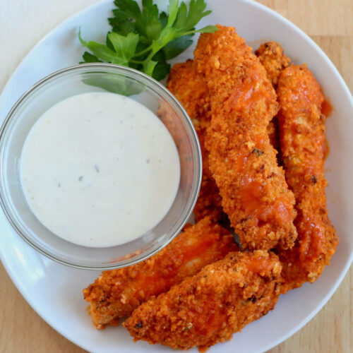 Air fryer buffalo chicken tenders on a small white plate next to a bowl of ranch dressing.