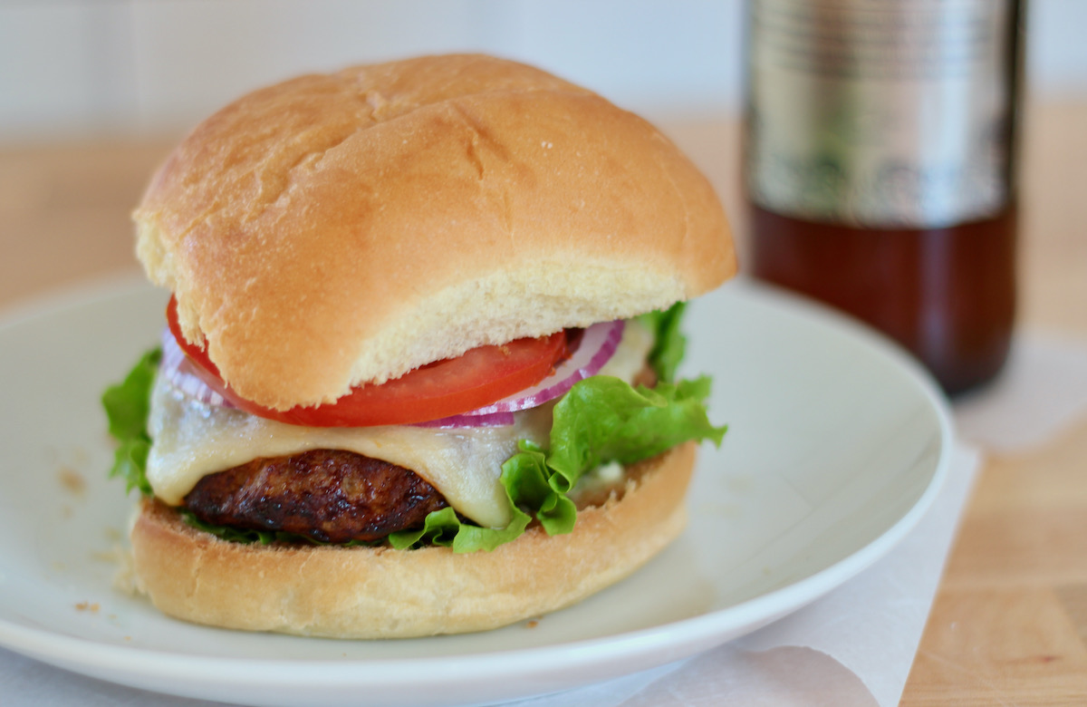 An air fryer turkey burger on a bun topped with cheese, tomato, red onion, and lettuce.