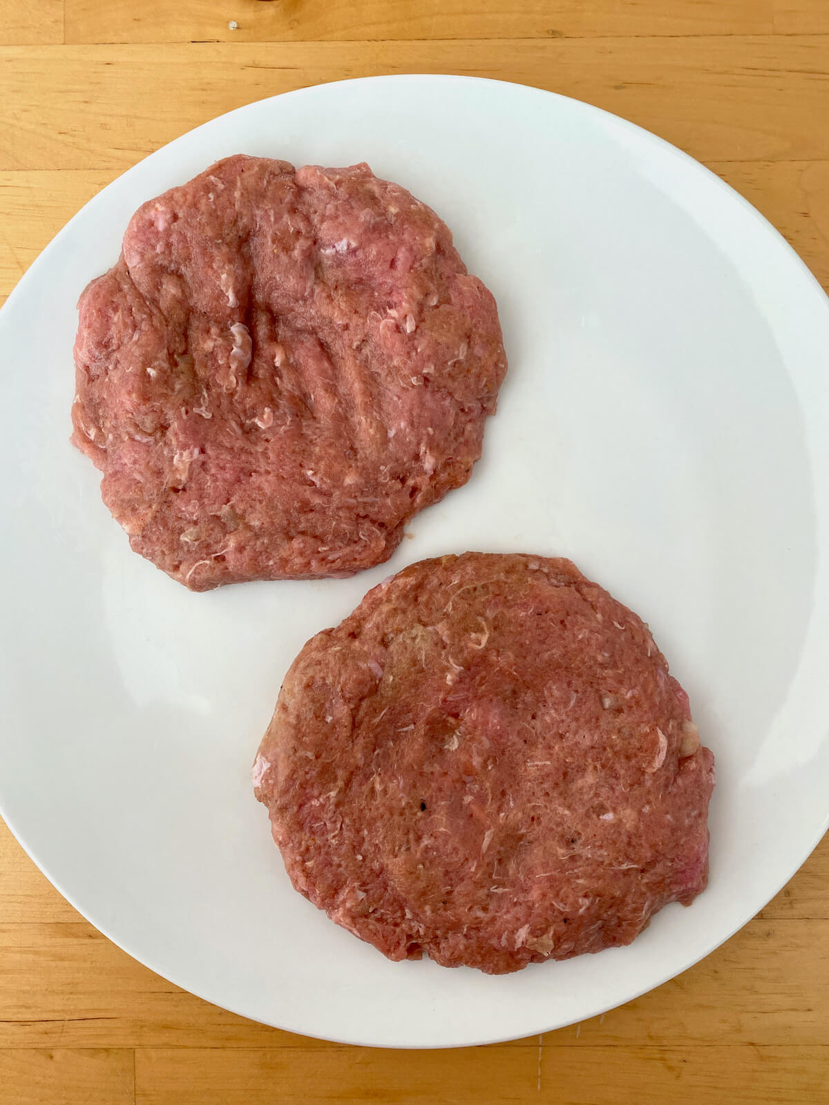 Two shaped turkey patties on a large white plate.