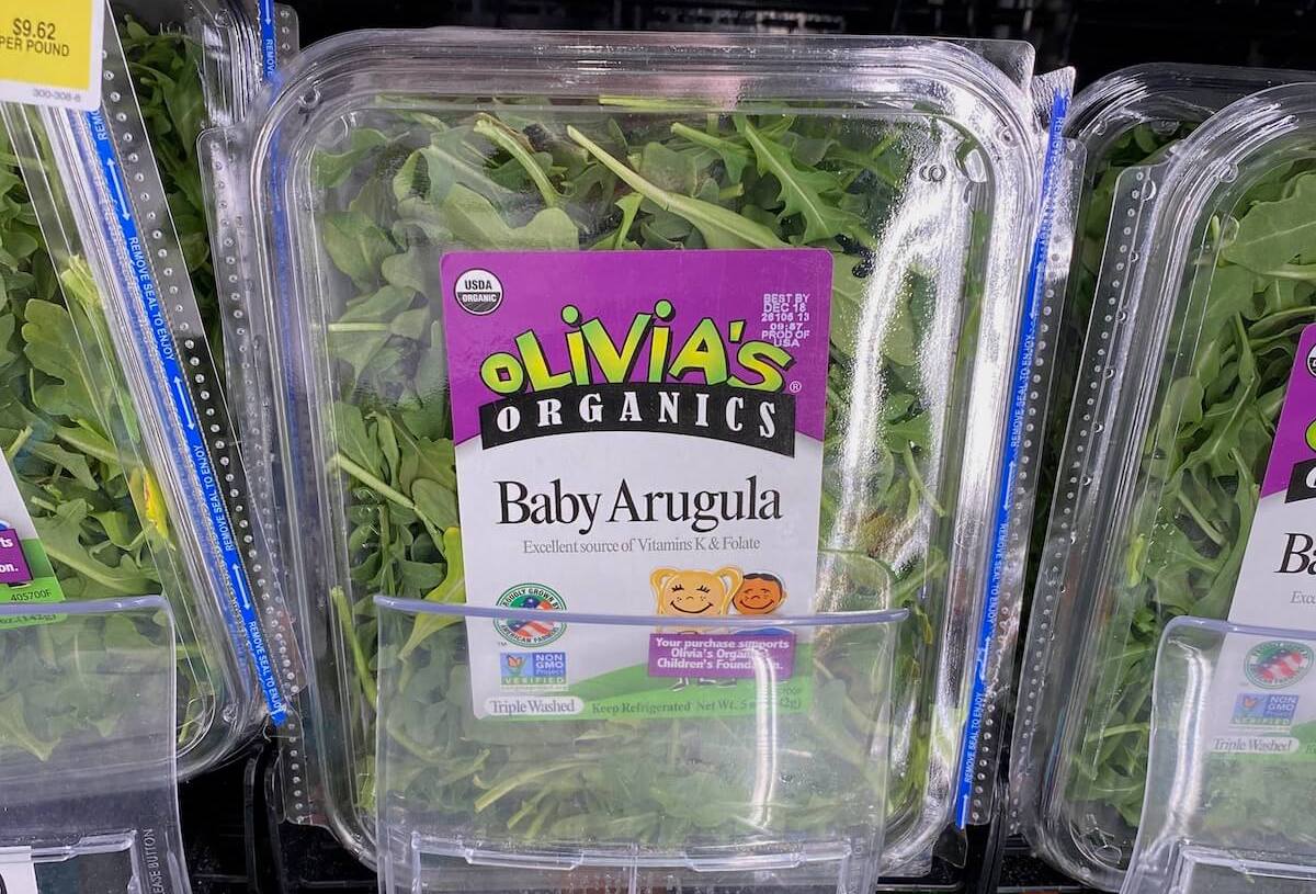 A plastic tub of baby arugula on a grocery store shelf.