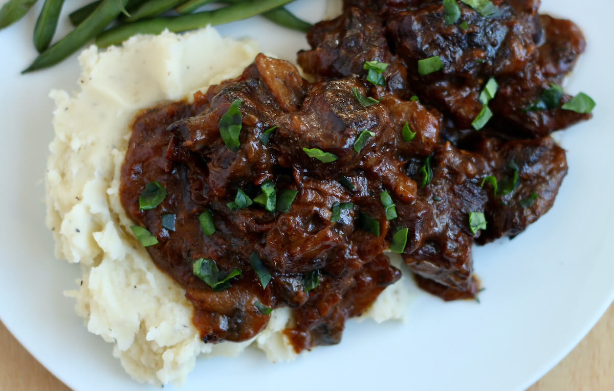 A serving of dutch oven steak tips on a pile of mashed potatoes.