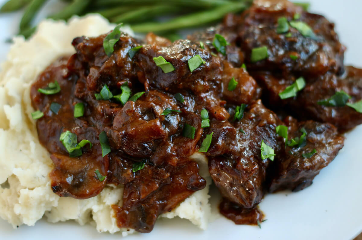 Dutch oven steak with mushroom gravy being served with mashed potatoes and green beans.