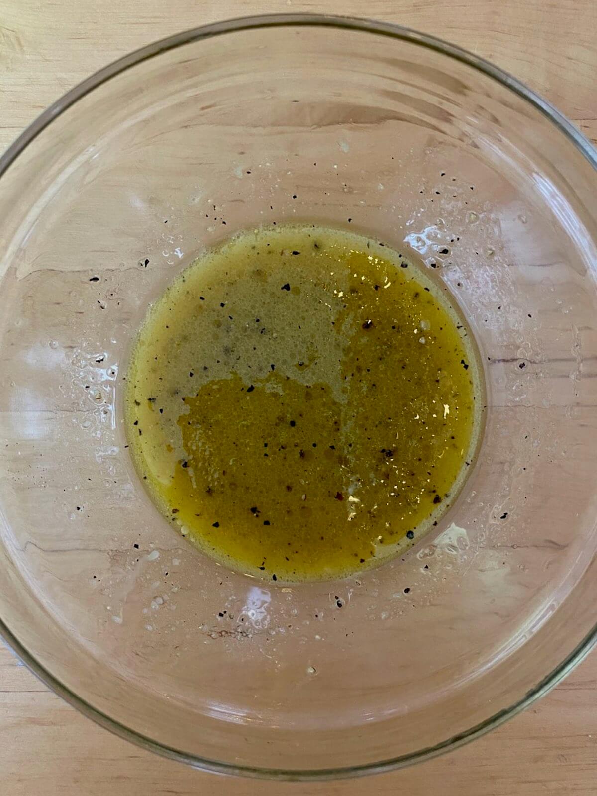 A small glass mixing bowl with maple dijon vinaigrette.